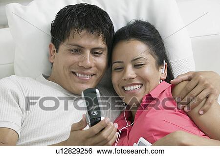 Couple lying on couch looking at picture on mobile phone close up View Large Photo Image Stock Photograph - Couple lying on couch looking at picture on mobile phone close up. Fotosearch