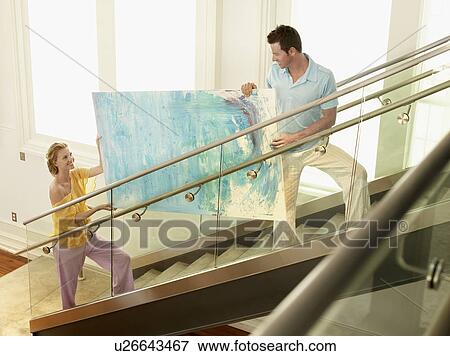 Stock Photo - Couple moving modern painting up stairs elevated view. Fotosearch