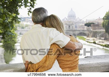 Stock Photograph - Couple on bridge in Rome Italy looking at view of cathedral back view. Fotosearch