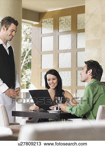 Stock Image - Couple ordering from waiter at outdoor restaurant. Fotosearch