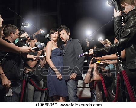 Stock Image - Couple posing on red carpet being photographed by paparazzi. Fotosearch