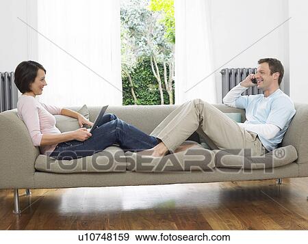 Couple reclining on couch using laptop and cell phone View Large Photo Image Stock Photo - Couple reclining on couch using laptop and cell phone. Fotosearch