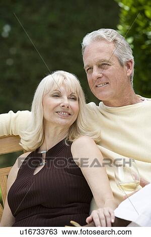 Stock Image - Couple relaxing on bench outdoors. Fotosearch