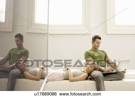 Couple relaxing together on sofa man using laptop View Large Photo Image Stock Photograph - Couple relaxing together on sofa man using laptop. Fotosearch