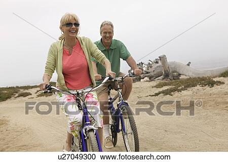 Stock Image - Couple riding bicycles along beach. Fotosearch