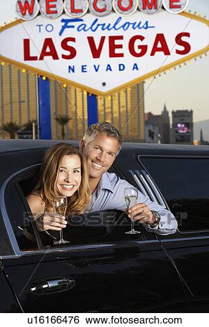 Stock Photograph - Couple sitting in limousine with drinking glasses in front of Welcome to Las Vegas sign. Fotosearch