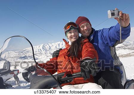 Couple sitting on snowmobile in snow photographing selves with digital camera. View Large Photo Image Stock Photo - Couple sitting on snowmobile in snow photographing selves with digital camera.. Fotosearch