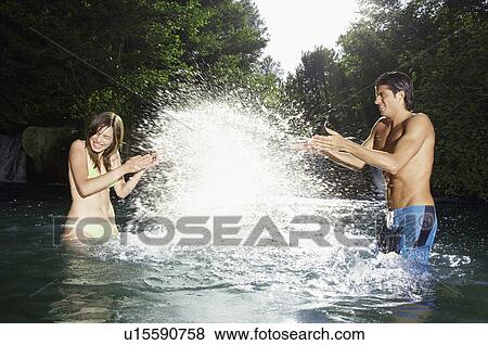 Stock Photo - Couple splashing water at each other in forest river side view. Fotosearch