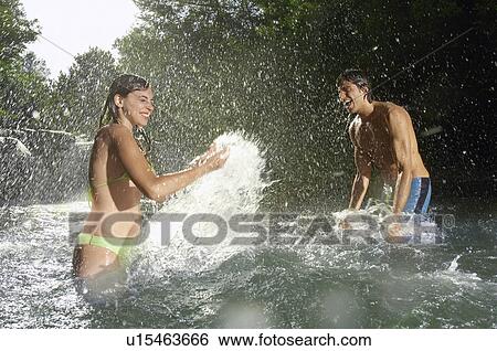 Stock Photograph - Couple splashing water at each other in forest river side view. Fotosearch