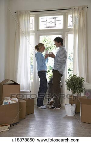 Stock Image - Couple standing by window surrounded by boxes. Fotosearch