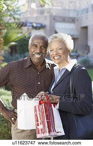 Stock Photo - Couple standing side by side outside with shopping bags on Shopping Trip. Fotosearch