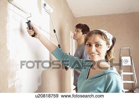 Couple using paint rollers on wall of living room View Large Photo Image Stock Photo - Couple using paint rollers on wall of living room. Fotosearch