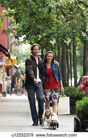 Stock Photo - Couple walking dog on sidewalk. Fotosearch