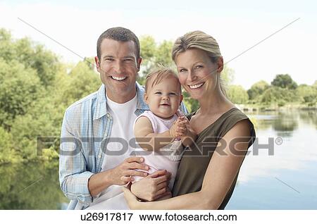Stock Photo - Couple with child standing by lake half length. Fotosearch
