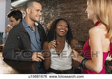 Couple with friend holding drinks laughing standing at bar View Large Photo Image Stock Photograph - Couple with friend holding drinks laughing standing at bar. Fotosearch