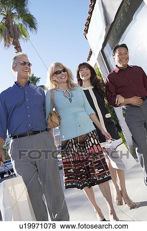 Stock Photo - Couples walking arm in arm outdoors on Shopping Trip. Fotosearch