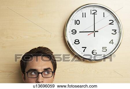 Stock Photo - Cropped image of young businessman in glasses looking up to office clock. Fotosearch