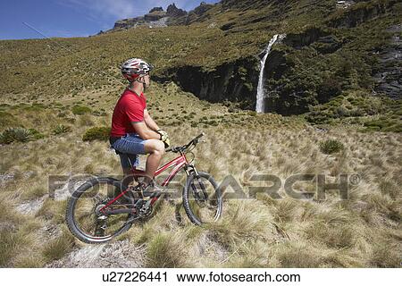 Stock Image - Cyclist looking at waterfall in field. Fotosearch