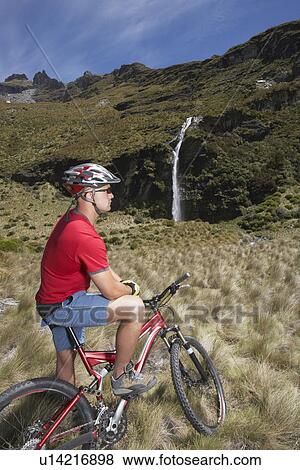 Stock Photo - Cyclist looking at waterfall in field. Fotosearch