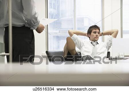 Picture - Disinterested businessman reclining on chair and ignoring boss in office. Fotosearch