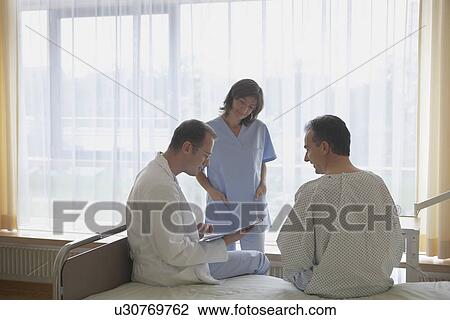 Stock Image - Doctor and Nurse Consulting with Patient in hospital room. Fotosearch