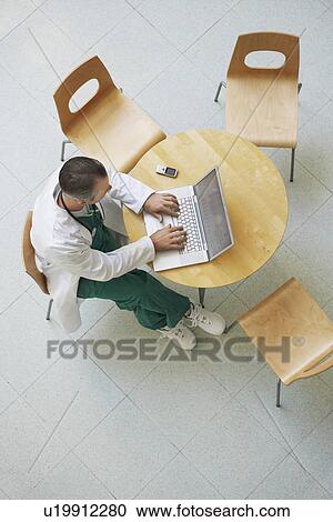Stock Image - Doctor Using Laptop in cafeteria view from above. Fotosearch