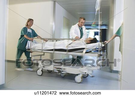 Stock Image - Doctors Moving Patient on gurney through hospital corridor. Fotosearch