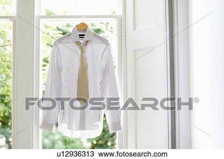 Stock Image - Dress shirt and tie on hanger in domestic window. Fotosearch