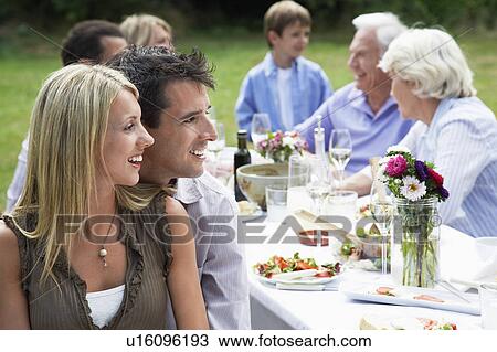 Stock Image - Family dining in garden focus on couple in foreground. Fotosearch