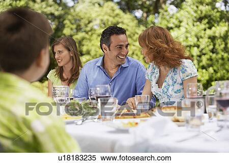 Stock Photography - Family having meal at table in back yard. Fotosearch