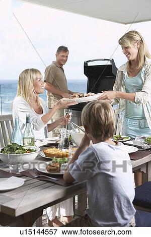 Family sitting around table outside eating Barbecue father standing at grill grilling View Large Photo Image Stock Photo - Family sitting around table outside eating Barbecue father standing at grill grilling. Fotosearch