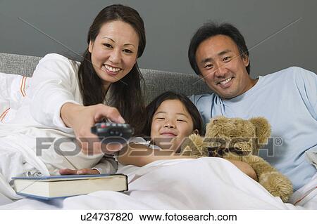 Stock Image - Family Watching TV Together in Bed mother using remote control. Fotosearch