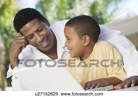 Stock Photo - Father and Son sitting on patio Using Laptop close up. Fotosearch