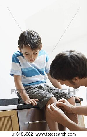 Stock Image - Father Applying plaster to knee of son. Fotosearch