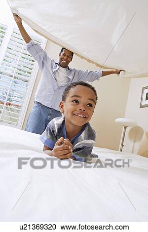 Stock Image - Father holding bed sheet over son (3-6). Fotosearch