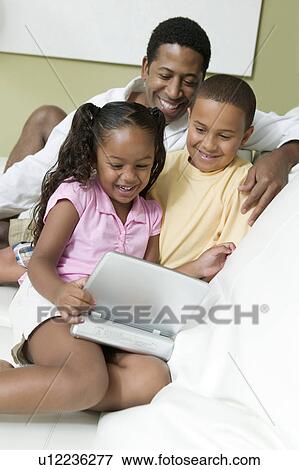 Stock Photo - Father son and Daughter on sofa Watching Movie on Portable DVD Player. Fotosearch