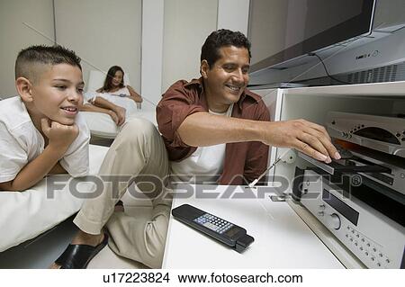 Picture - Father with son Putting Disc in DVD Player in living room. Fotosearch