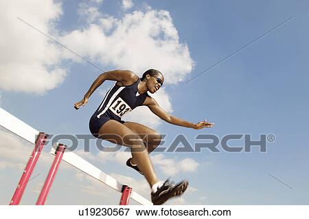 Stock Photo - Female athlete jumping hurdle. Fotosearch