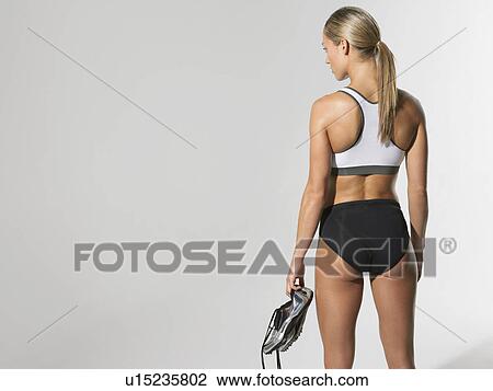 Female athlete standing holding shoes back view View Large Photo Image Stock Image - Female athlete standing holding shoes back view. Fotosearch