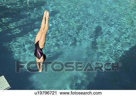 Stock Image - Female diver diving into pool mid air. Fotosearch