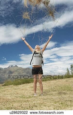 Stock Image - Female hiker throwing grass into air in field. Fotosearch