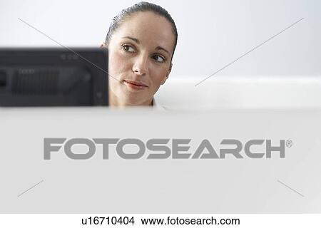 Picture - Female office worker sitting behind monitor in office cubicle. Fotosearch