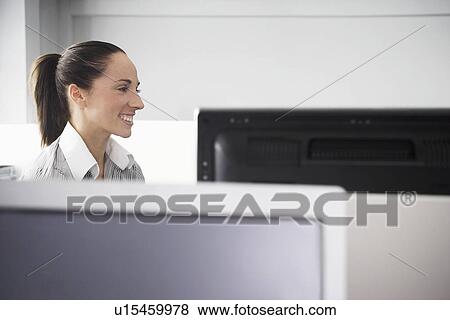 Stock Photo - Female office worker sitting in office cubicle smiling. Fotosearch