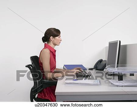 Stock Image - Female office worker using computer at desk in office. Fotosearch