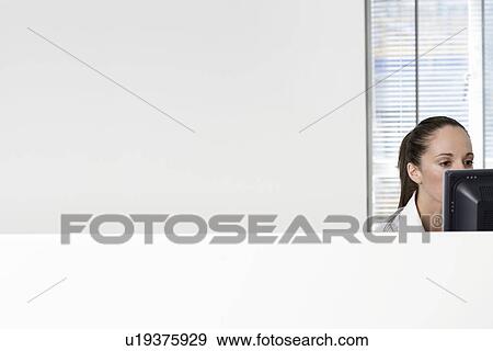 Stock Photo - Female office worker using computer in office cubicle. Fotosearch