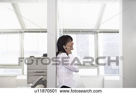 Female office worker using mobile phone leaning against column in office side view View Large Photo Image Stock Image - Female office worker using mobile phone leaning against column in office side view. Fotosearch