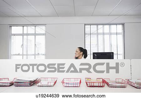 Female office worker using telephone smiling in office cubicle behind trays with documents View Large Photo Image Stock Photo - Female office worker using telephone smiling in office cubicle behind trays with documents. Fotosearch