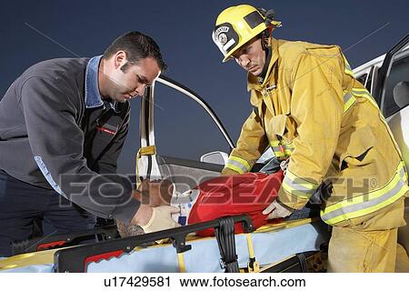 Stock Image - Fire fighter and paramedic assisting man at crash site. Fotosearch