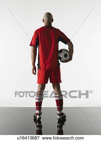 Stock Photo - Football player standing holding ball back view. Fotosearch
