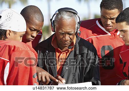 Stock Photo - Football players surrounding coach on field. Fotosearch